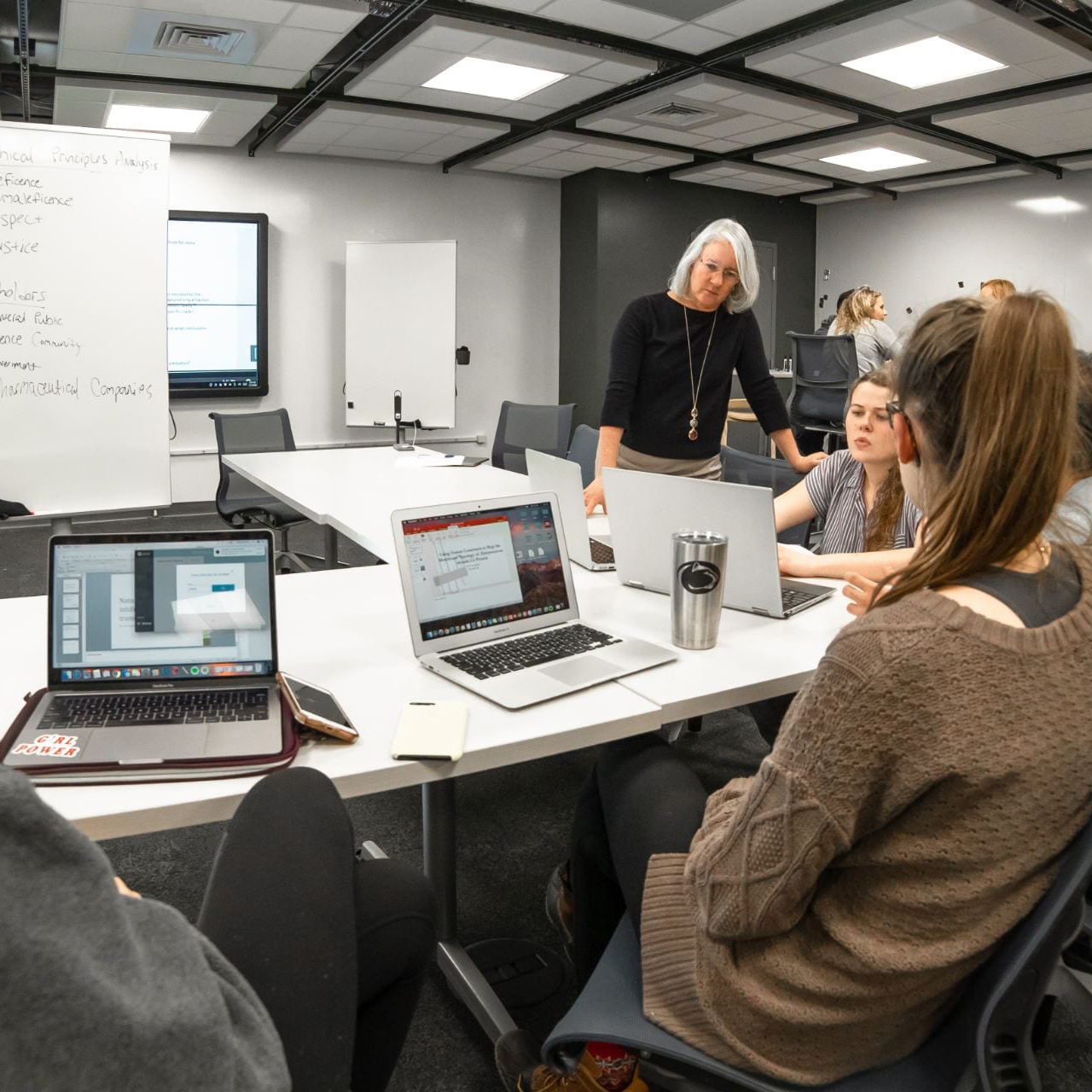 LearningSpaces An instructor leans on writeable tables and talks to a group of collaborating students